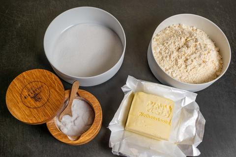 Zutaten für Mürbeteig: Butter, Zucker, Mehl und Salz auf schwarzem Untergrund. Das Ei Fehlt noch