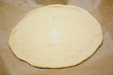 Hefeteig auf dem Backpapier geformt zur Pizza
