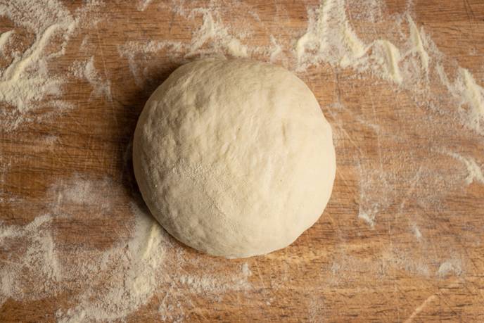 Runde glatte Pizzateig-Kugel auf bemehltem Holzbrett