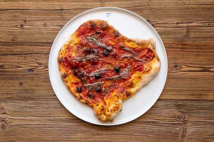 Sardellen-Pizza mit Tomatensauce, Sardellenfilets, Oliven und Oregano auf weißem Teller